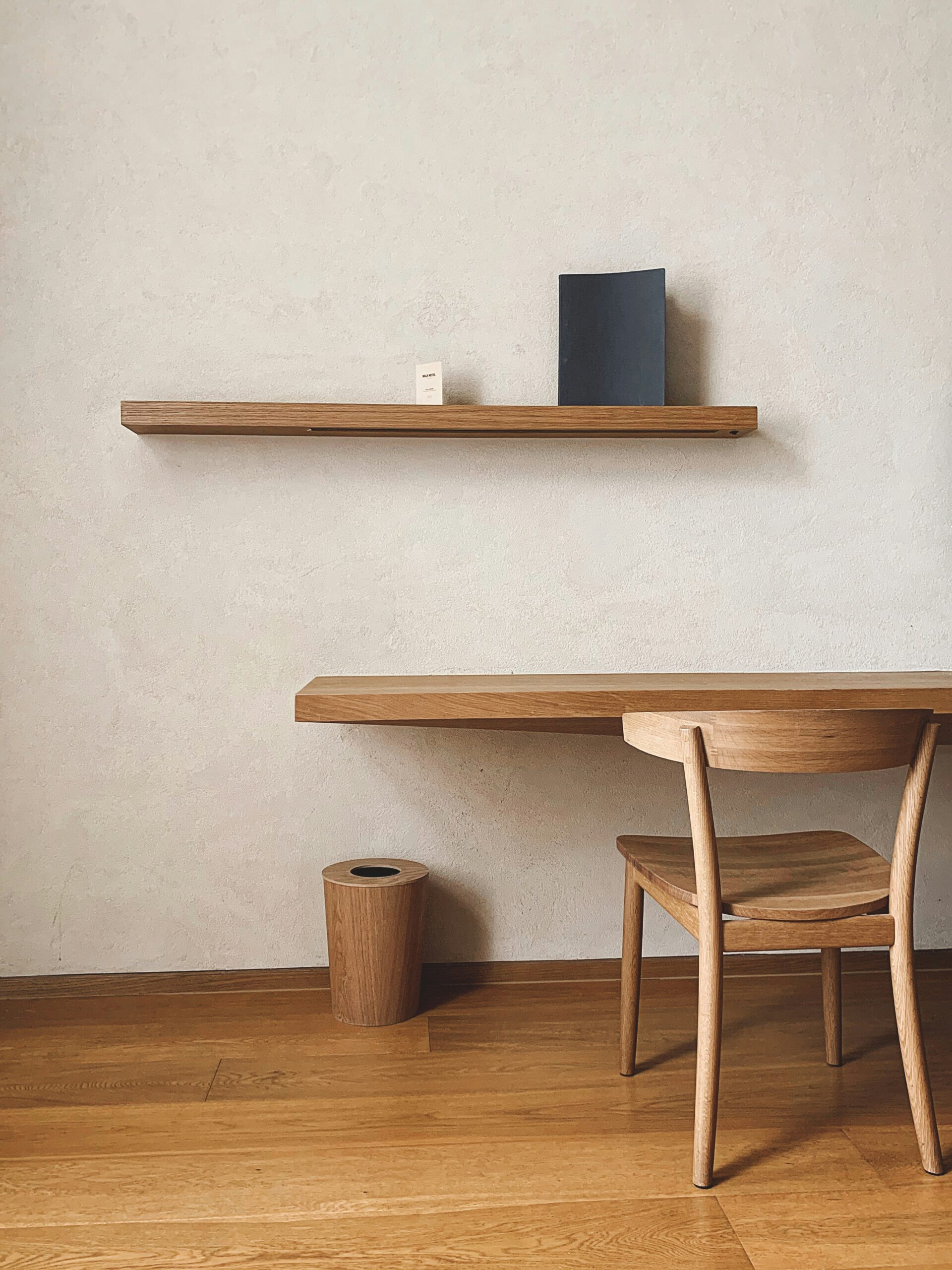 Mobilier en bois moderne avec une table et une chaise, sur fond de mur texturé et étagère minimaliste.