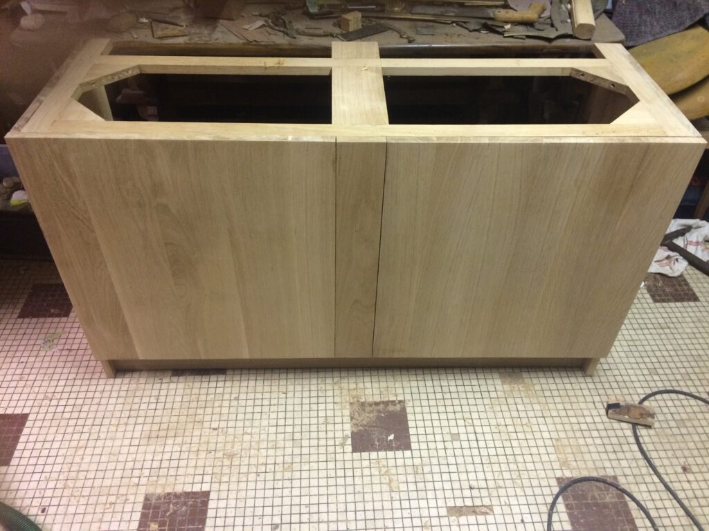 Meuble en bois brut en cours de restauration, avec partie supérieure découpée pour un évier, dans un atelier d'ébénisterie.