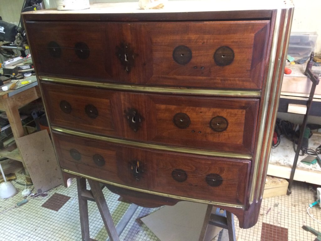 Commode Régence en placage d’amarante, avec trois tiroirs et des finitions en laiton, dans un atelier de restauration.