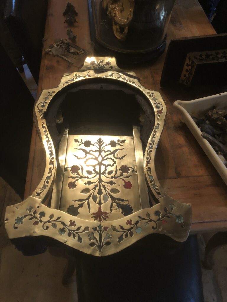 Cartel XVIII en marqueterie Boulle, ornée de motifs floraux, sur une table en bois.