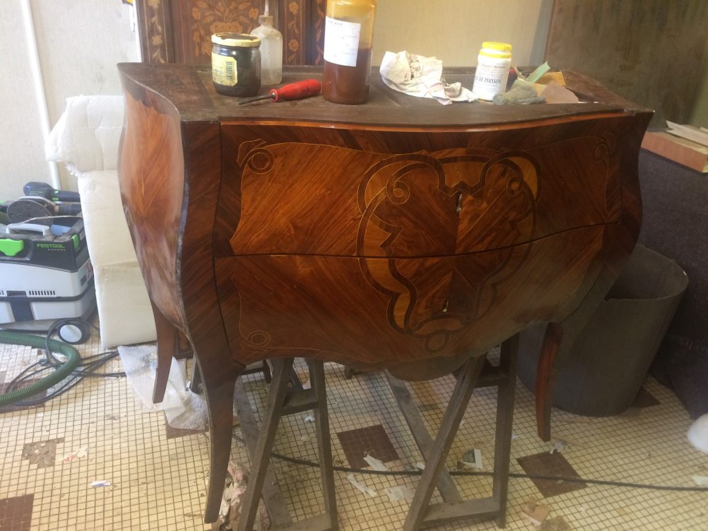 Commode Louis-XV en placage de bois de rose, sur socle de travail, avec outils et produits de restauration à proximité.