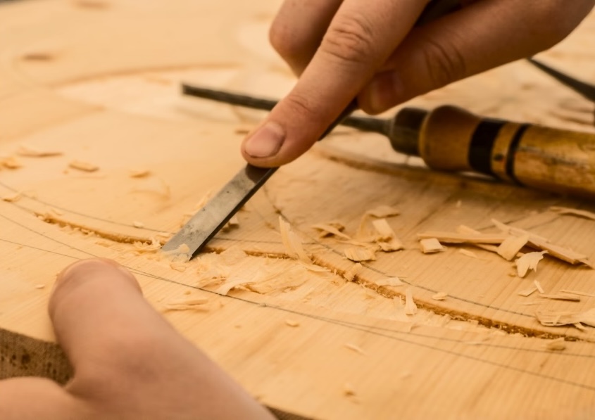 Main en train de sculpter du bois, mettant en avant le savoir-faire de l'ébéniste dans la rénovation de mobilier ancien.