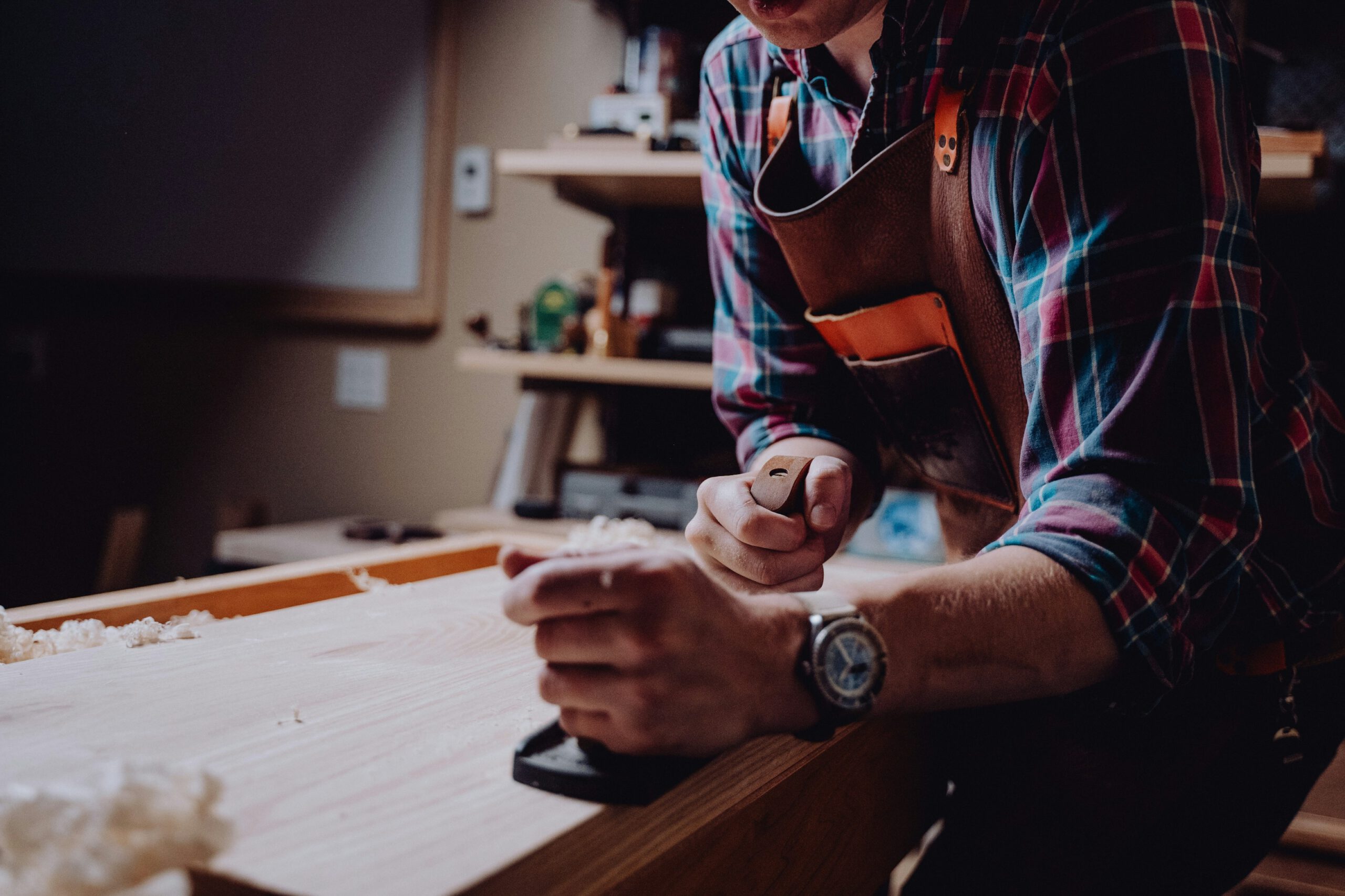 Artisan au travail, utilisant un outil de précision sur une planche de bois, dans un atelier de menuiserie.